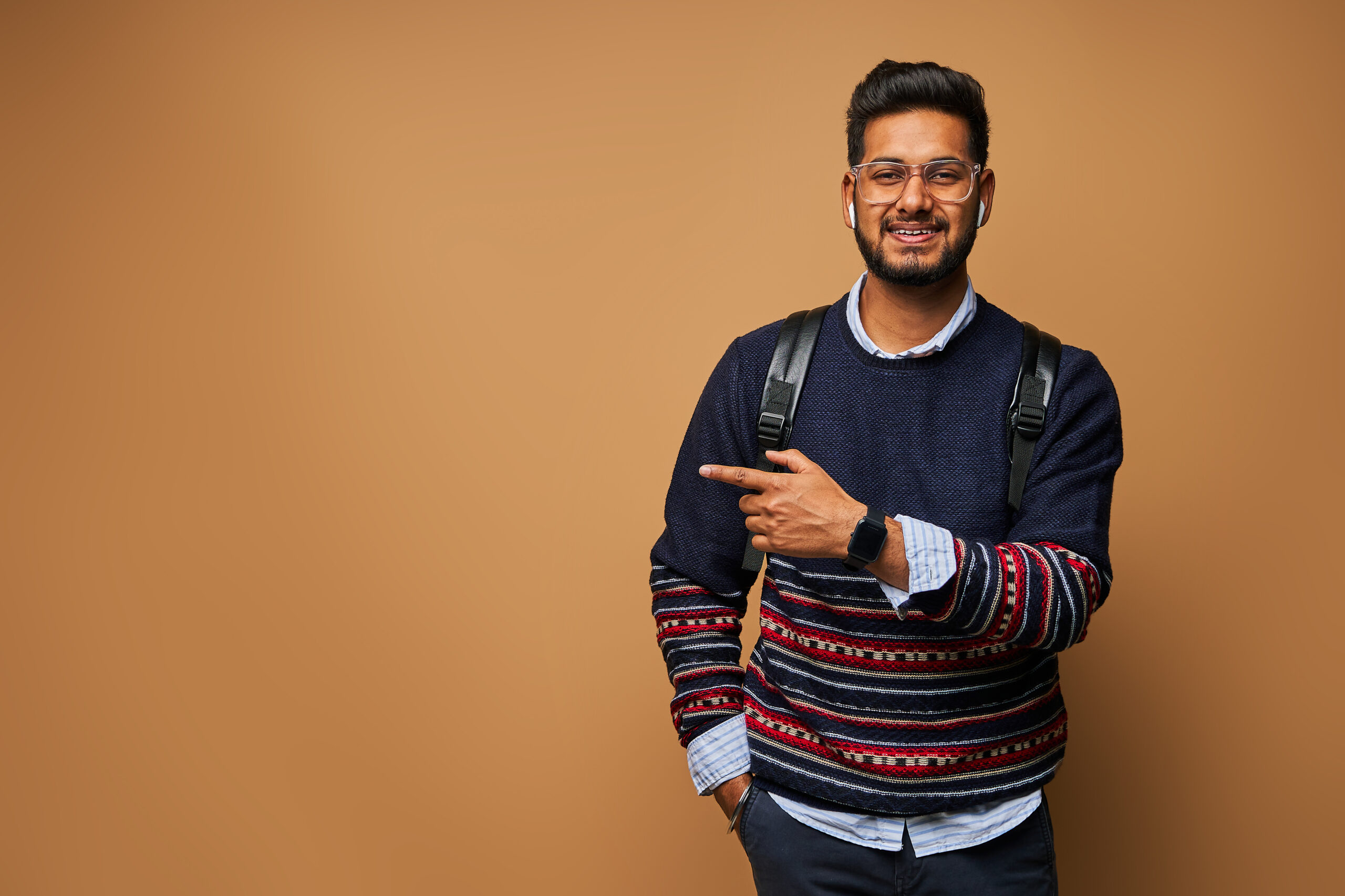 smiling happy indian student with backpack pointing his finger o